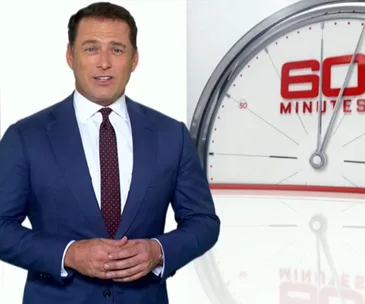 Man in a suit stands before a "60 Minutes" logo and clock background.