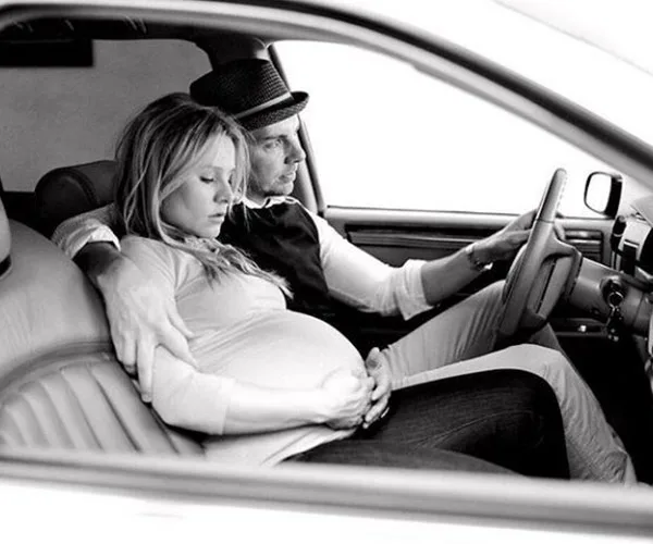 Pregnant woman and man in a car, man driving while embracing her, monochrome photo.