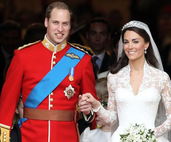 Wedding couple exiting ceremony; groom in red military uniform, bride in lace gown with veil, holding bouquet.