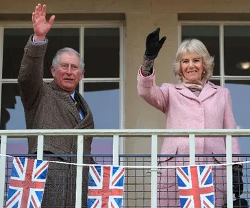Two people waving on a balcony with British flags hanging below.