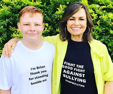 Two people smiling; one wearing a shirt saying "I'm Brian" and the other supporting anti-bullying. Green leafy background.