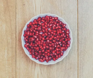 Bowl of fresh red pomegranate seeds on a wooden table.