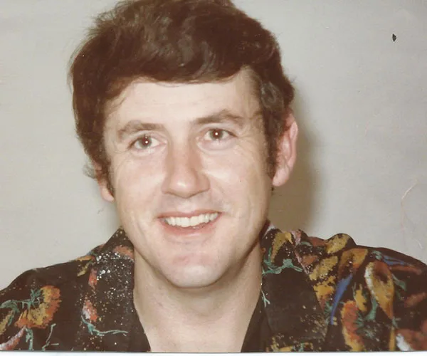 Man smiling in a colorful shirt with a neutral background.