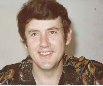 Man smiling in a colorful shirt with a neutral background.