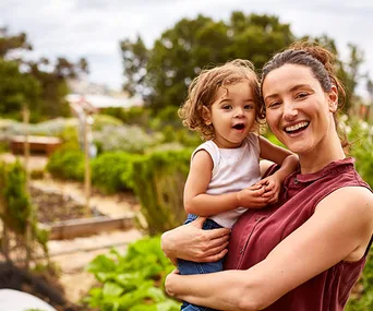 Smiling woman holding a toddler in an outdoor garden.