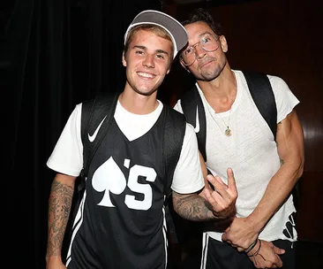 Two individuals smiling, one wearing a cap and sports jersey, the other in glasses and a white shirt, posing together.