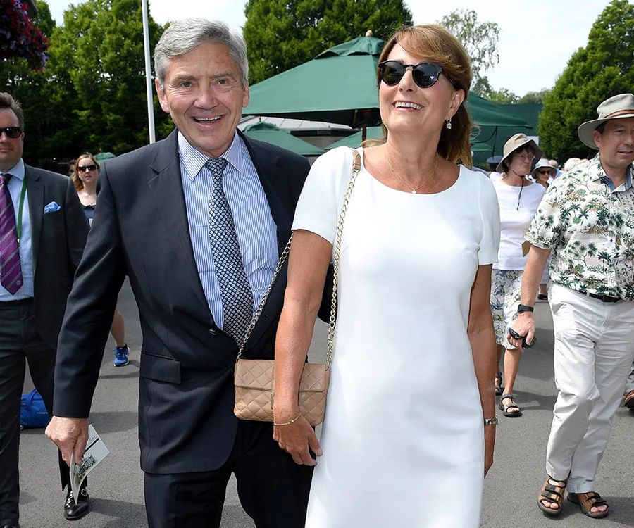 A smiling couple in summer attire walking outdoors with people and greenery around them.