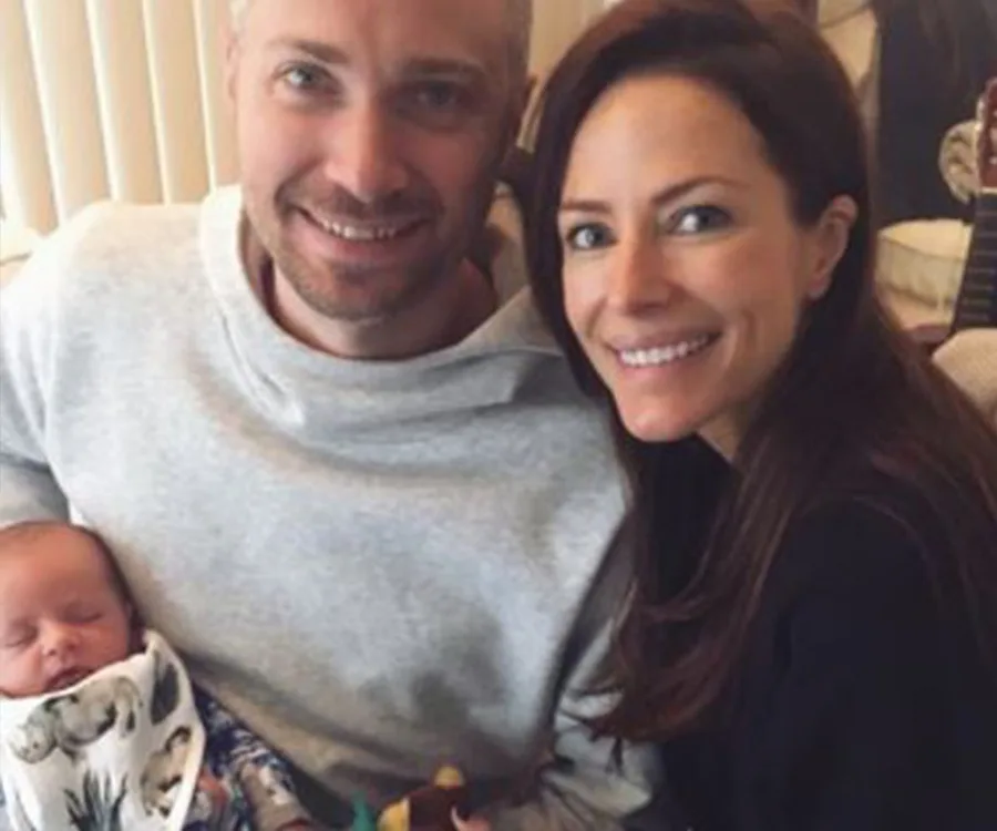 A smiling couple poses with their newborn baby wrapped in a printed blanket.