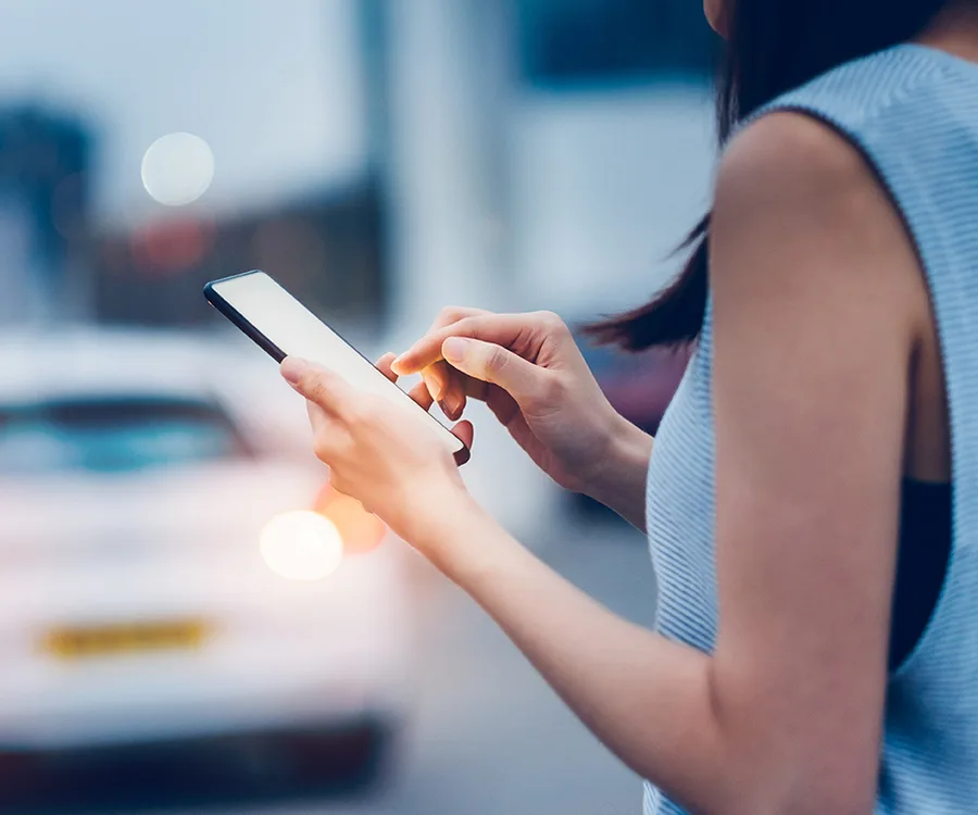 A woman using a smartphone on a city street, with blurred background lighting.