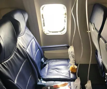 Airplane cabin with missing window frame, oxygen masks deployed, and empty seats in disorder.