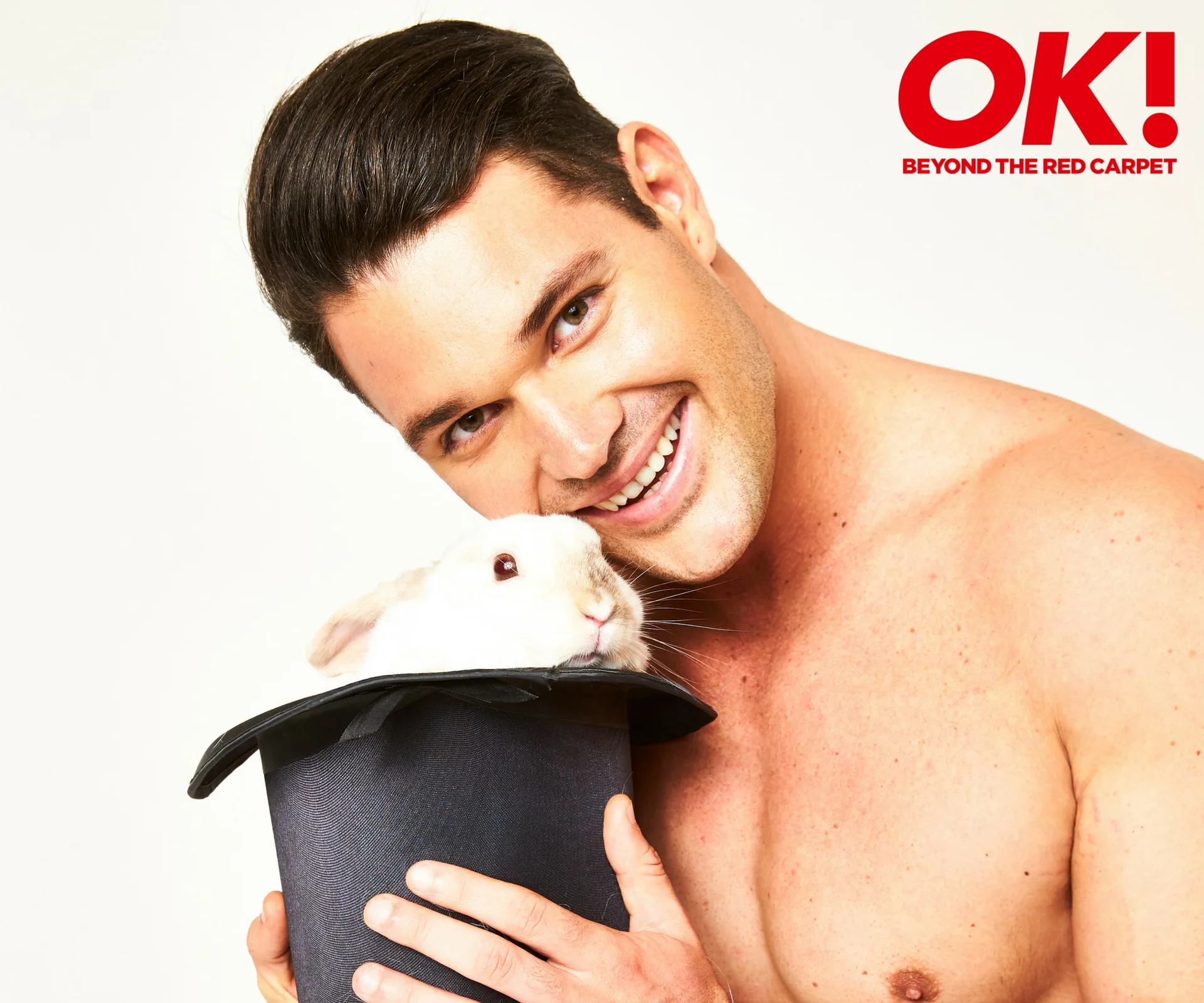 Shirtless man smiling while holding a rabbit in a hat; OK! magazine logo in the corner.