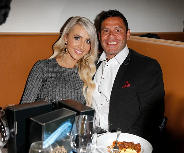 A couple smiling and seated at a restaurant table, with food and drinks in view.