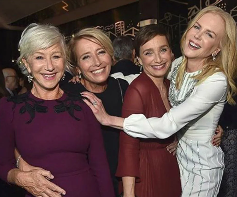 Four women smiling and hugging at an event, dressed in formal attire.