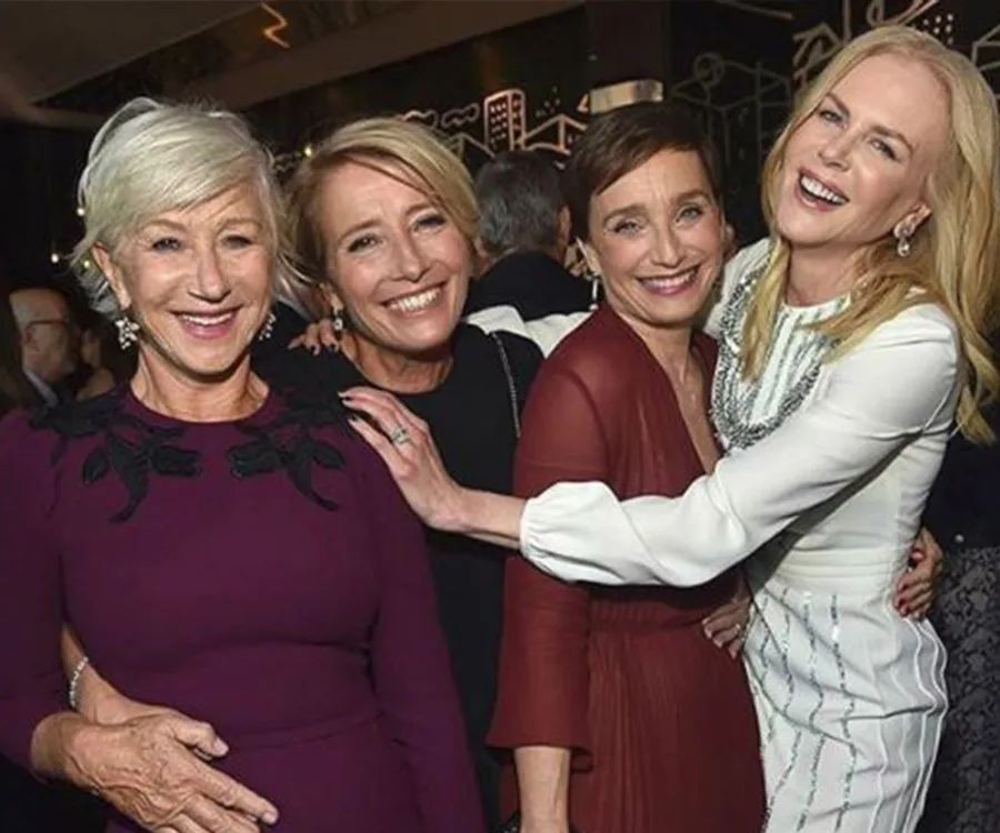 Four women smiling and hugging at an event, dressed in formal attire.
