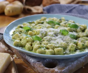 Plate of homemade gnocchi with basil pesto and grated cheese on a wooden board.