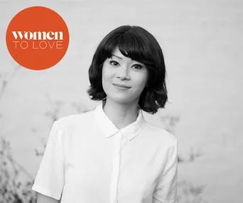 Black and white portrait of a woman in a white shirt, with "Women to Love" logo in orange.