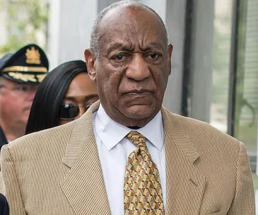 A man in a striped suit and patterned tie outside a building, flanked by others, looking serious.