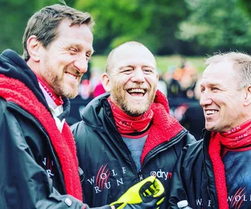 Three men laughing together outdoors, wearing Wolf Run jackets and red scarves.