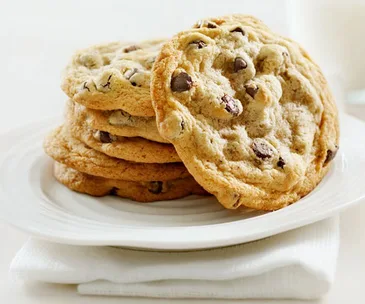 A stack of freshly baked chocolate chip cookies on a white plate, placed on a folded napkin.