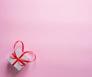 A small polka-dot gift box with a red ribbon on a pink background.