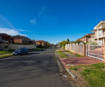 Residential street with houses and a parked car under a clear blue sky.