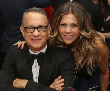 Couple smiling at a formal event, man in glasses and tuxedo, woman with long hair in a dress.