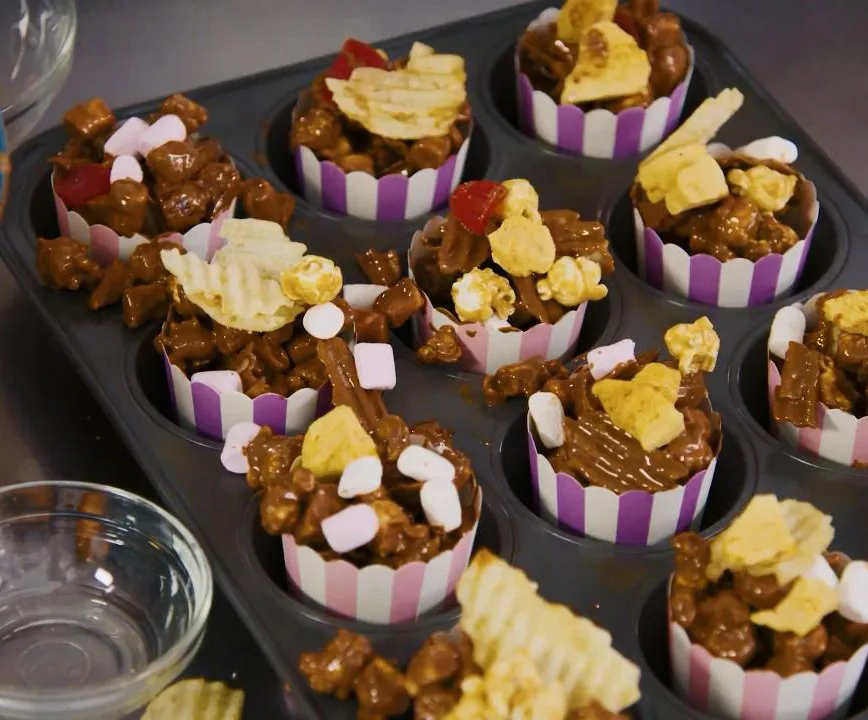 Barbie-themed popcorn cups with toppings like marshmallows and chips in striped baking cups.