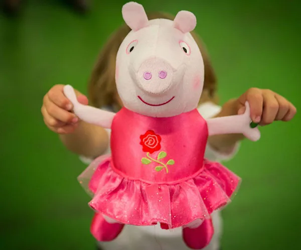 Child holding Peppa Pig plush toy in a pink dress with a rose, against a green background.