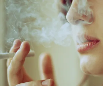 Person smoking cigarette with smoke surrounding their face.