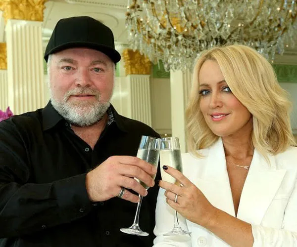 Two people toasting with champagne glasses in a luxurious setting with a chandelier in the background.