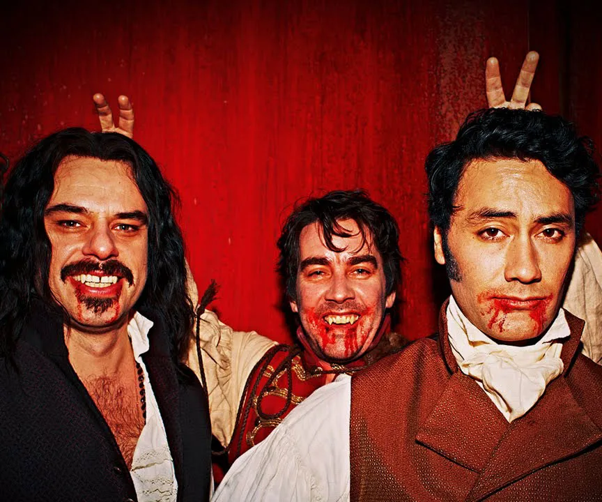 Three characters from "What We Do in the Shadows" with vampire costumes and blood on faces, posing for a playful photo.