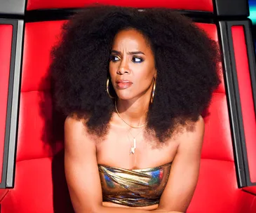 Judge on "The Voice" in a reflective dress, sitting in a red chair, with a thoughtful expression.
