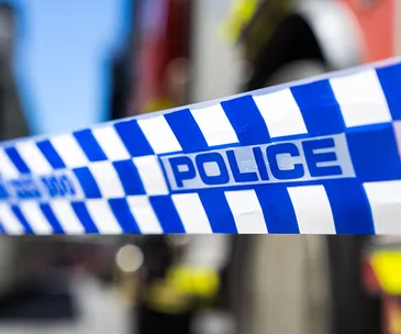 Police tape cordoning off an area, with blurred emergency response vehicles in the background.
