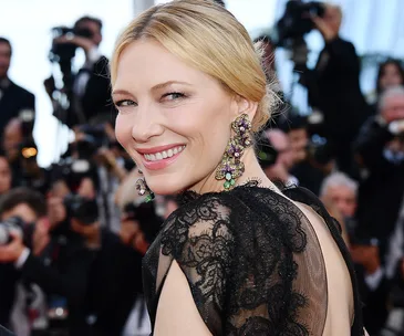 A person in a black lace gown with colorful statement earrings smiles at Cannes Film Festival 2018.