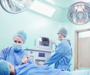 Medical team in surgical scrubs with a patient in an operating room, focusing on a procedure.
