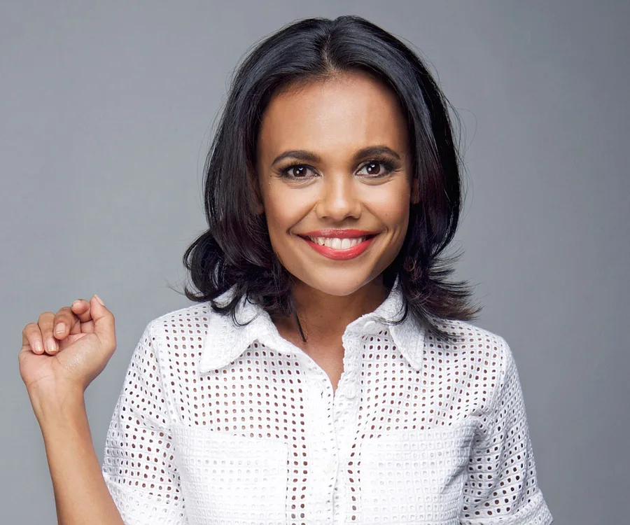 A smiling woman with dark hair in a white patterned blouse against a grey background.