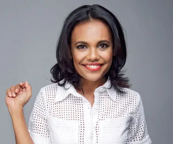 A smiling woman with dark hair in a white patterned blouse against a grey background.