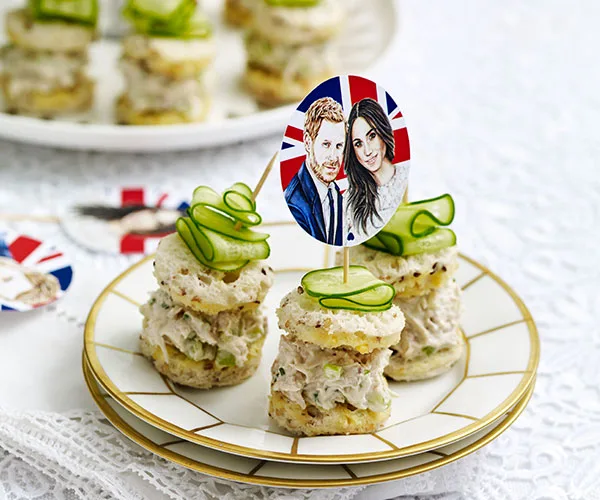 Mini sandwiches topped with cucumber slices, decorated with a toothpick showing a couple against a Union Jack background.