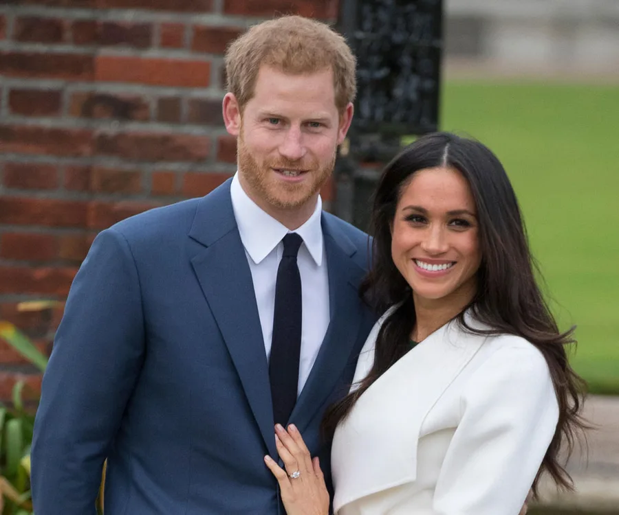 A couple smiling outdoors, the man in a blue suit and the woman in a white coat, standing close together.