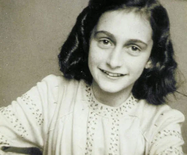 Young girl with dark hair smiling softly, wearing a light-colored blouse with embroidered patterns, against a plain background.