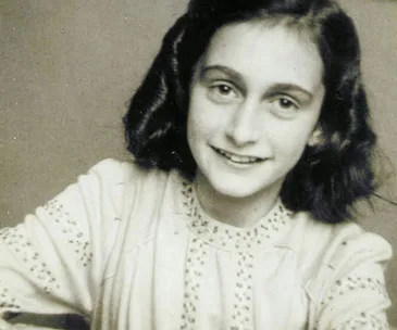 Young girl with dark hair smiling softly, wearing a light-colored blouse with embroidered patterns, against a plain background.