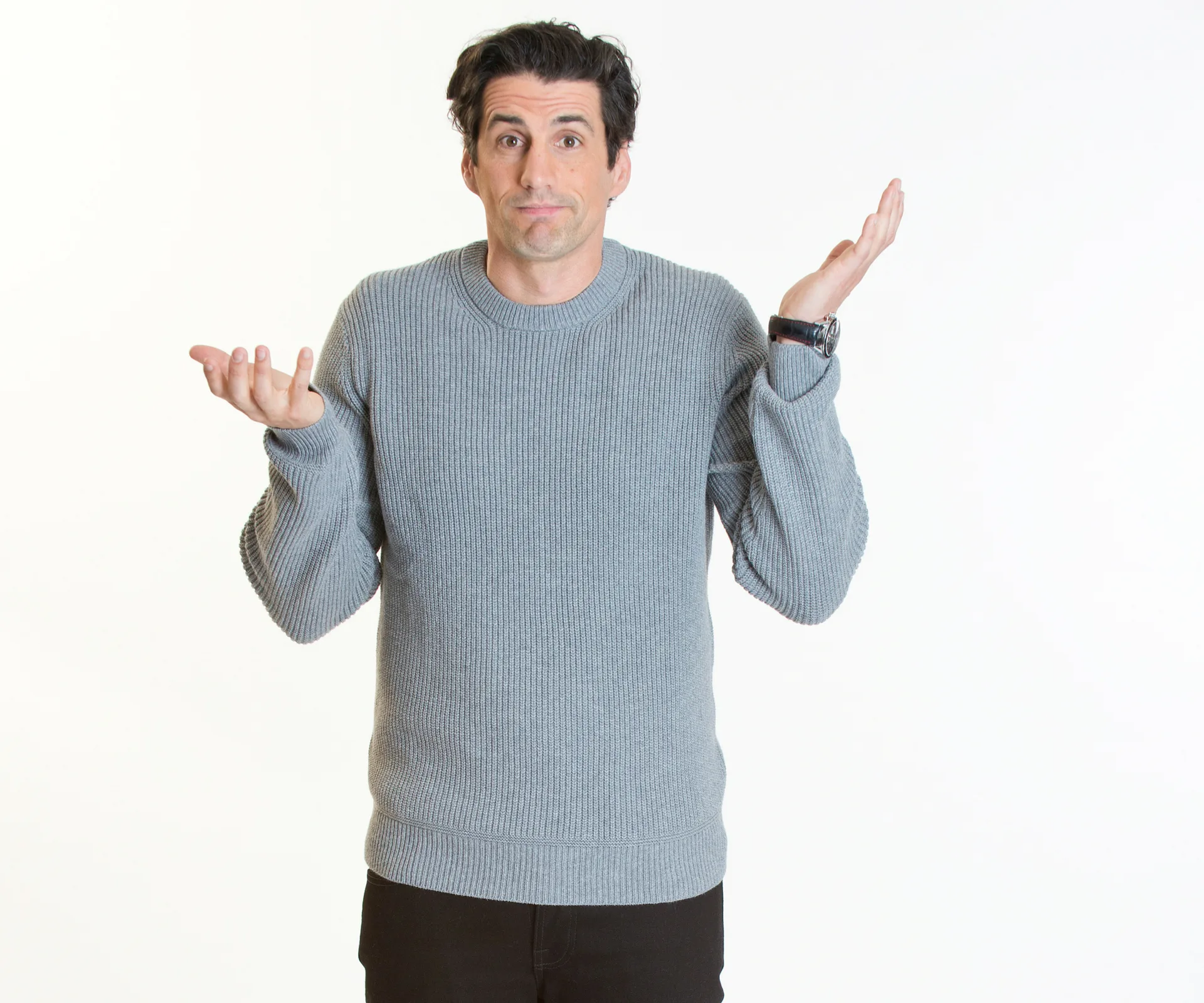 A man in a gray sweater shrugging with arms raised, expressing uncertainty against a white background.