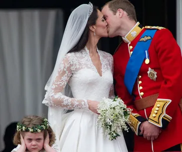 Bride and groom kiss, while a flower girl covers her ears with an unhappy expression.