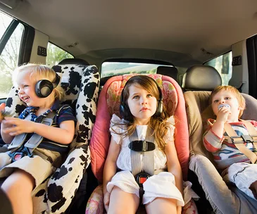 Three children in car seats wearing headphones, sitting safely in the back of a vehicle.