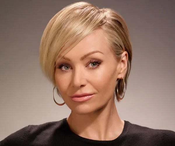 Portia de Rossi with short blonde hair and hoop earrings, wearing a black top against a plain background.