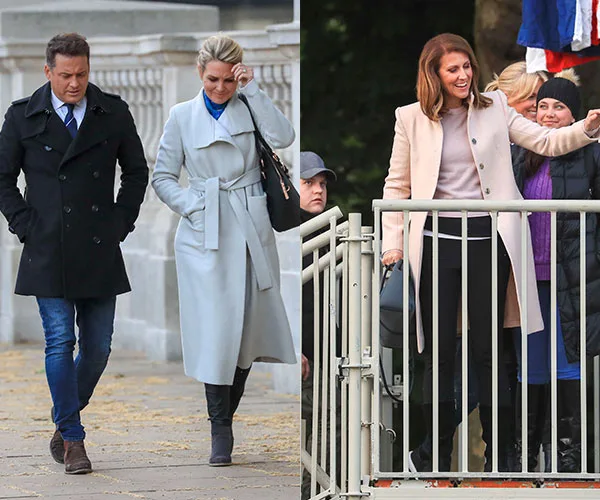 Two people in coats walking outside on the left; a woman in a beige coat, smiling, and waving on the right.