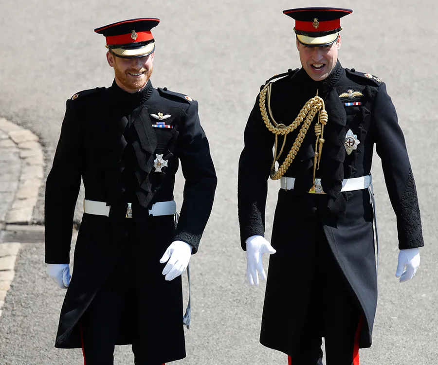 Two men in formal military attire walking outdoors, both wearing black uniforms with red and gold accents.