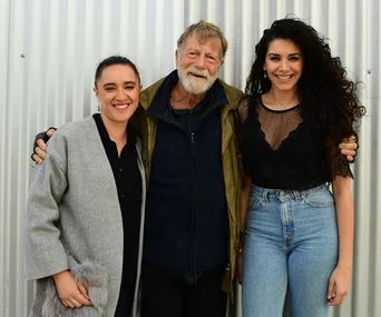Group photo of three smiling people, two women and a man, standing in front of a corrugated metal background.