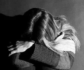 A woman with long hair sits with her head down on her arms, creating a somber and introspective mood.