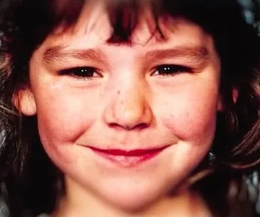 Young girl smiling with soft lighting, brown hair, and rosy cheeks.